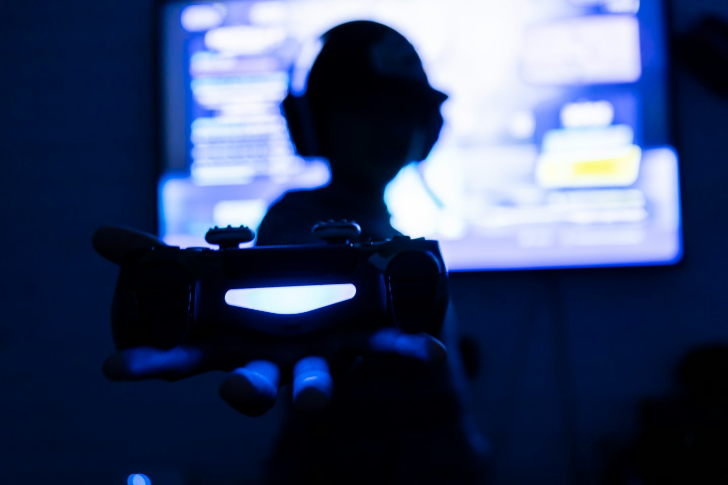 Silhouette holding a glowing blue video game controller.