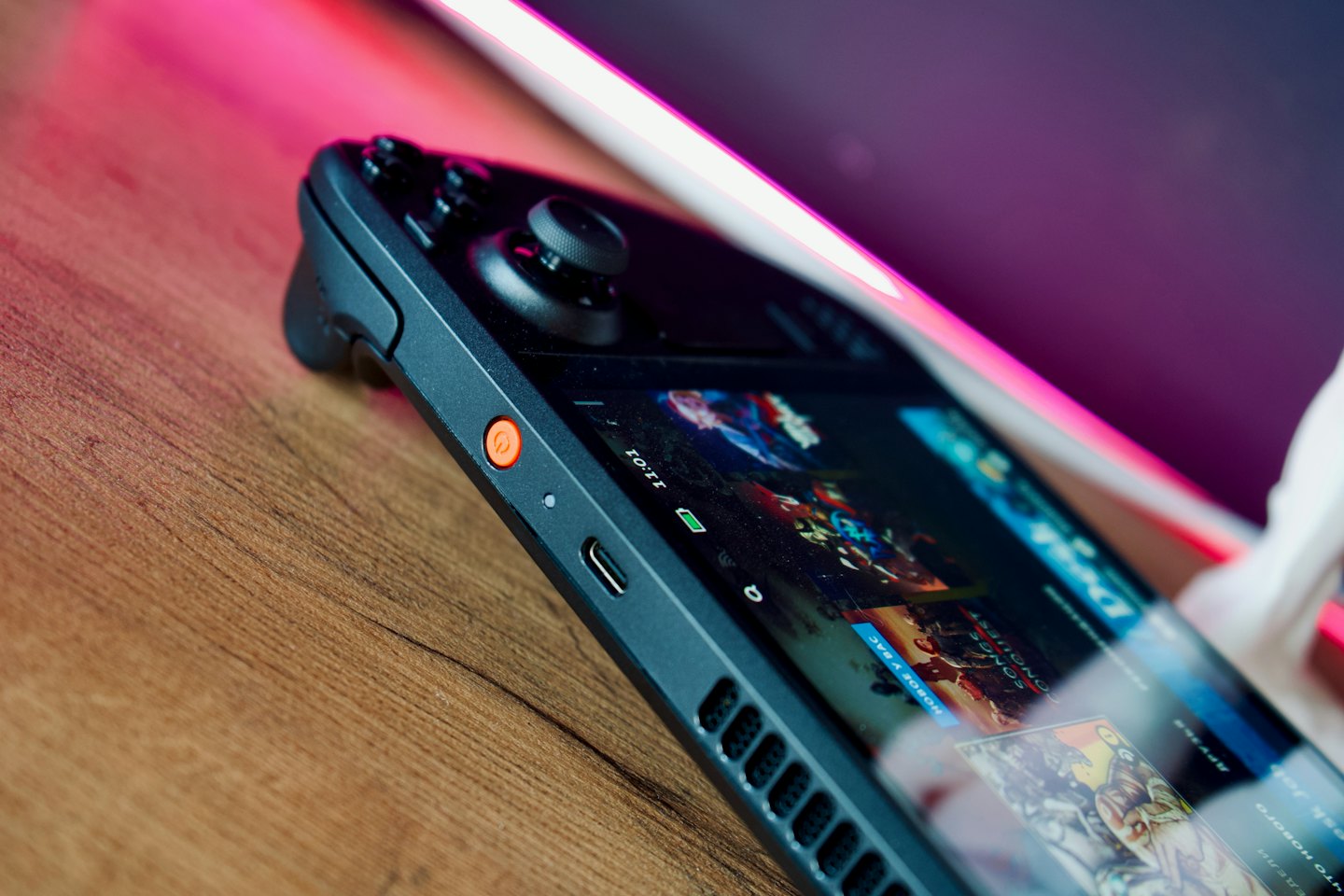A black handheld gaming console rests on a wooden desk.