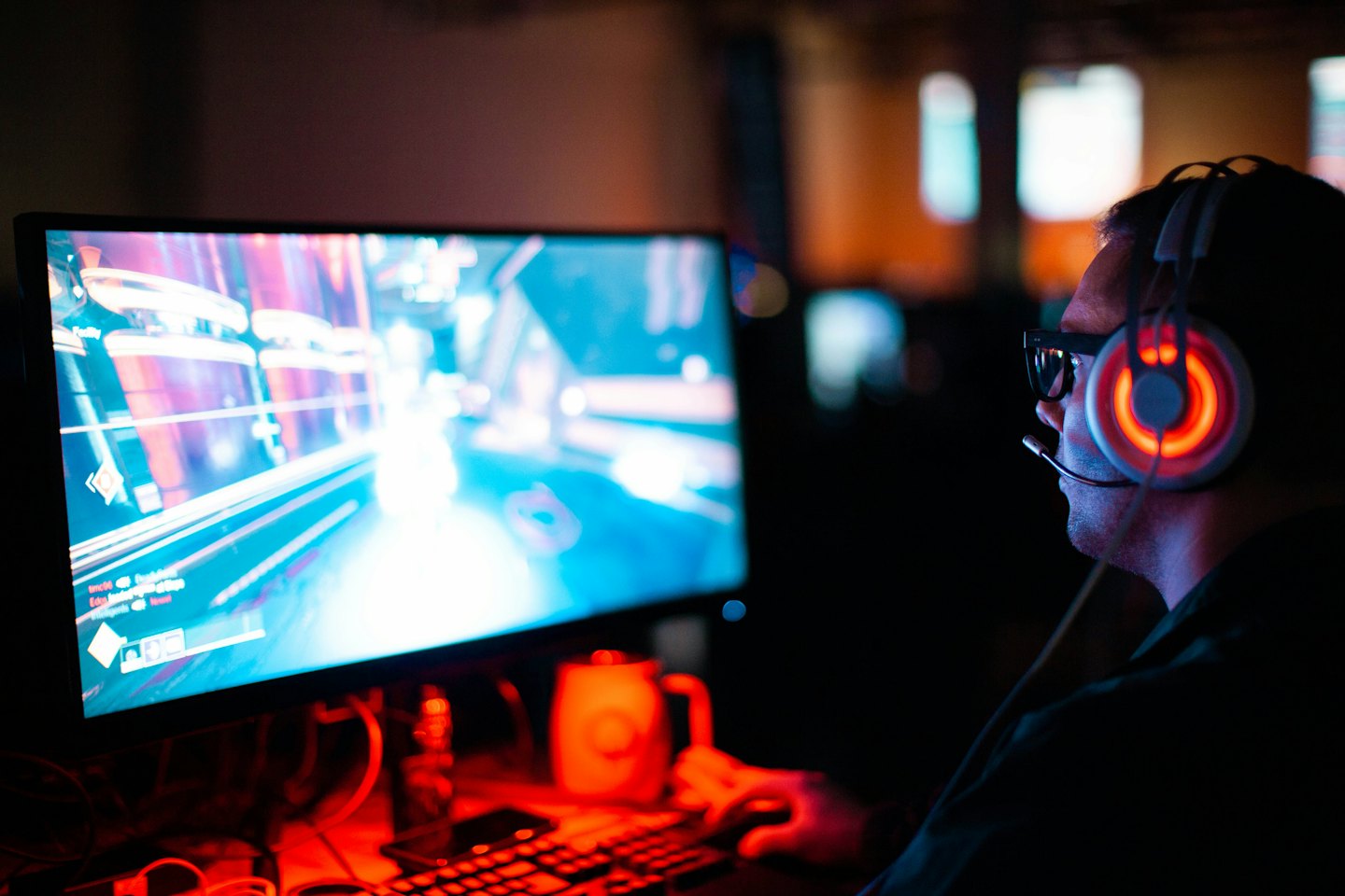Gamer wearing a headset plays video games on a glowing computer screen.